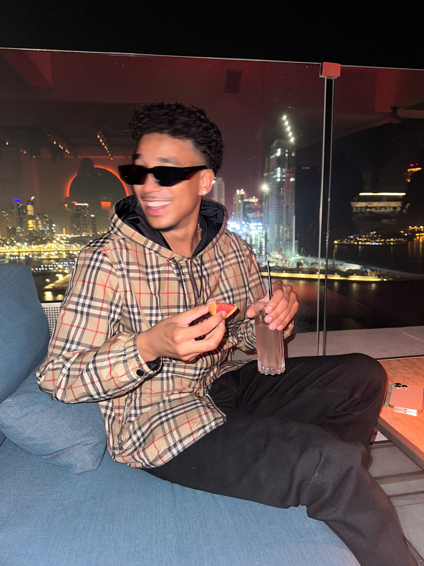 Dubai, 2024 — The Smile of Someone Who Knows What's Coming Joshua Arthur JJ smiling Dubai skyline at night wearing Burberry luxury empire building 2024 JJDREAMSS resurrection
